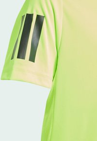 T-shirt de sport vert néon avec des manches courtes, une texture lisse et trois rayures verticales noires sur la manche gauche.