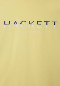Żółta bawełniana koszulka z krótkim rękawem z napisem "HACKETT LONDON" w granatowym i białym kolorze, umieszczonym na środku przodu. Gładka faktura.
