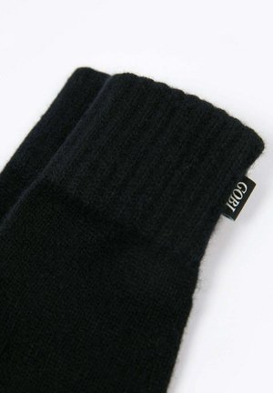 Schwarze gestrickte Wollhandschuhe mit gerippten Bündchen und einem kleinen Stoffetikett an der Seite.