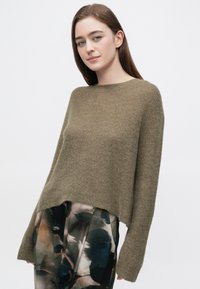 Pulover tricotat verde măsliniu, cu croială lejeră, guler rotund și mâneci lungi, asortat cu pantaloni largi, cu model.