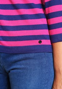 Randig stickad topp i rosa och marinblå, med horisontella ränder. Avslutad med en liten svart detalj vid fållen. Buren med blå denimjeans.