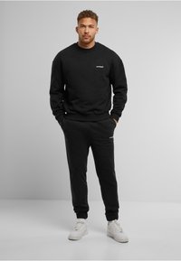 Zwart sweatshirt- en joggingbroekset, met een ronde hals, ribgebreide manchetten en zoom, en een klein logo op de borst. Gecombineerd met witte sneakers.