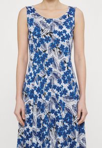 Robe sans manches avec un motif floral bleu sur fond blanc, agrémentée d'accents de feuilles noires et d'un corsage ajusté qui s'évase à l'ourlet.