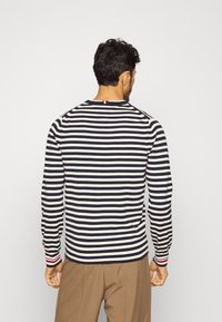 Chemise à manches longues rayée bleu marine et blanche, dotée d'un col rond et d'un accent rouge et blanc sur les poignets. Texture de tissu lisse.