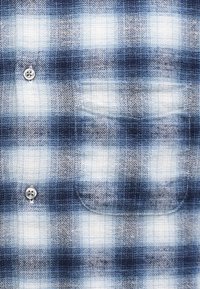 Πουκάμισο καρό με μπλε, άσπρους και γκρίζους τόνους. Φτιαγμένο από φλις, διαθέτει μια ραμμένη τσέπη και ασημένια κουμπιά για κλείσιμο.
