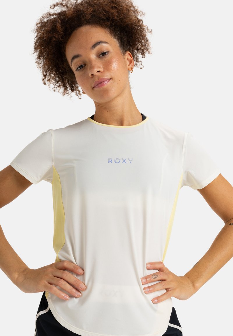 Camiseta atlética blanca con acentos laterales amarillos, cuello redondo, mangas cortas y logo bordado "ROXY" en el pecho. Tejido suave y ligero.
