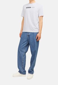 White cotton t-shirt with black “JACK & JONES” logo, paired with loose-fitting blue denim jeans and white sneakers.