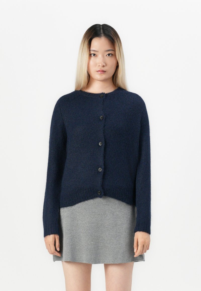 Cardigan en laine bleu marine à manches longues, avec un col rond et six fermetures à boutons, surface texturée et ourlet court.