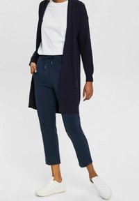 Granatowy sweter z dzianiny z otwartym przodem, sparowany z granatowymi joggerami z mankietami i białymi trampkami. Tekstura swetra zawiera wzór.
