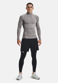 Přiléhavý šedý dlouhý rukáv s vysokým límcem, černé kraťasy a černé legíny. Bílé sportovní boty. Logo Under Armour na oblečení.
