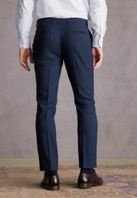 Marineblaue maßgeschneiderte Hose mit glatter Textur, schlanker Passform und zwei Gesäßtaschen. Kombiniert mit braunen polierten Schuhen.
