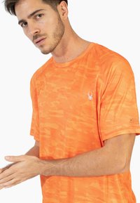 Camiseta deportiva naranja con una superficie texturizada y con patrón. Las mangas cortas y el cuello redondo presentan un logo sutil en el pecho.