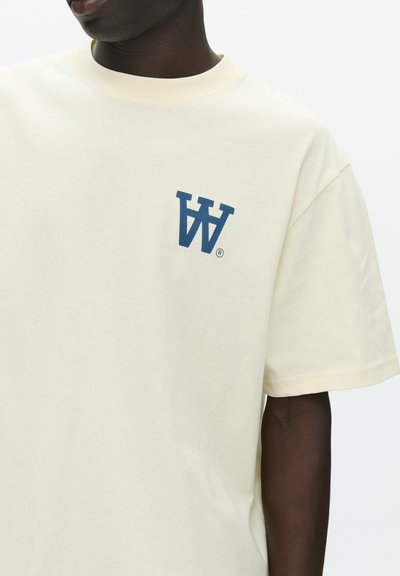 Κρεμ βαμβακερό t-shirt με σκούρο μπλε λογότυπο "W" στο αριστερό στήθος. Κοντά μανίκια και στρογγυλή λαιμόκοψη.