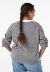 Harmaa neulepusero pyöreällä kaula-aukolla, ribbailluilla hihoilla ja helmalla. Tekstuurin näyttää pehmeältä ja mukavalta. Yhdistetty vaaleansinisiin farkkuihin.