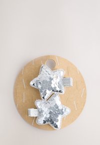 Zwei silberne Haarspangen mit Pailletten in Sternform auf einer runden braunen Pappunterlage mit Loch, verziert mit hellen Garnakzenten.