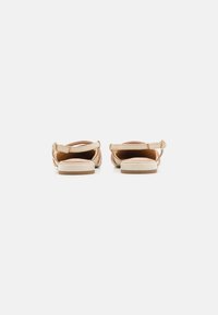 Tan sandals with a woven upper, adjustable ankle strap, and a flat sole. The design features a smooth texture and minimal detailing.