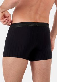 Mustat bokserit, joissa on teksturoitu ribbikuvio ja sileä, kiiltävä musta vyötärö. Materiaali näyttää joustavalta ja vartalonmyötäiseltä.