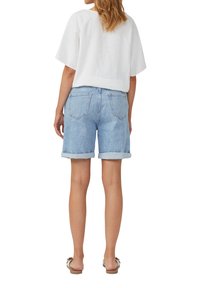 Helle blaue Denim-Shorts mit umgeschlagenen Säumen und einem weißen Leinen-Oberteil mit kurzen Ärmeln, von hinten betrachtet. Einfache Nähte und zwei Gesäßtaschen.