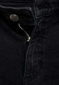 Jean en denim noir avec une fermeture éclair argentée partiellement ouverte et un bouton en métal visible sur la ceinture.