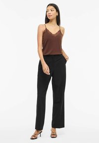 Brązowa koszulka na ramiączkach z koronkową lamówką, zestawiona z wysokimi czarnymi spodniami, dopełniona czarnymi sandałkami na paski. Prosty, elegancki design.