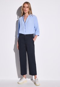 Ljusblå skjorta med uppvikta ärmar, kombinerad med svarta vida byxor och vita sneakers. Slät tyg med minimal detaljering.