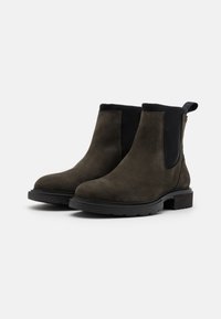 Bottines Chelsea en suede gris foncé avec des panneaux élastiques noirs sur les côtés, bout arrondi et semelle en caoutchouc plate. Dispose d'une languette en tissu au talon.
