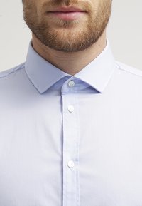 Camicia button-up azzurro chiaro con colletto classico, caratterizzata da bottoni bianchi e una trama liscia e tessuta.