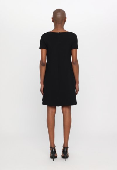 Black short-sleeved dress with a round neckline and a back zipper. Slightly flared shape, smooth texture, paired with black high-heeled shoes.