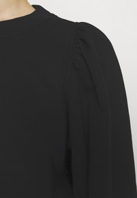 Svart topp med rund halsringning och puffärmar i ribbat material. Tyget verkar mjukt och elastiskt.