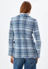 Blå och vit rutig blazer i textilerad tyg med slitna kanter. Har en klassisk krage och en strukturerad passform.