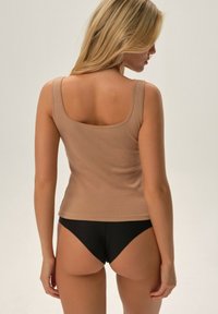 Light tan ribbed tank top with square neck and narrow straps, paired with black bikini bottom. Smooth texture, fitted design.