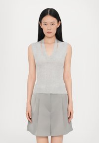 Top senza maniche grigio a coste con scollatura a V e dettagli a taglio, realizzato in materiale morbido. Abbinato a pantaloni corti plissettati grigio chiaro.