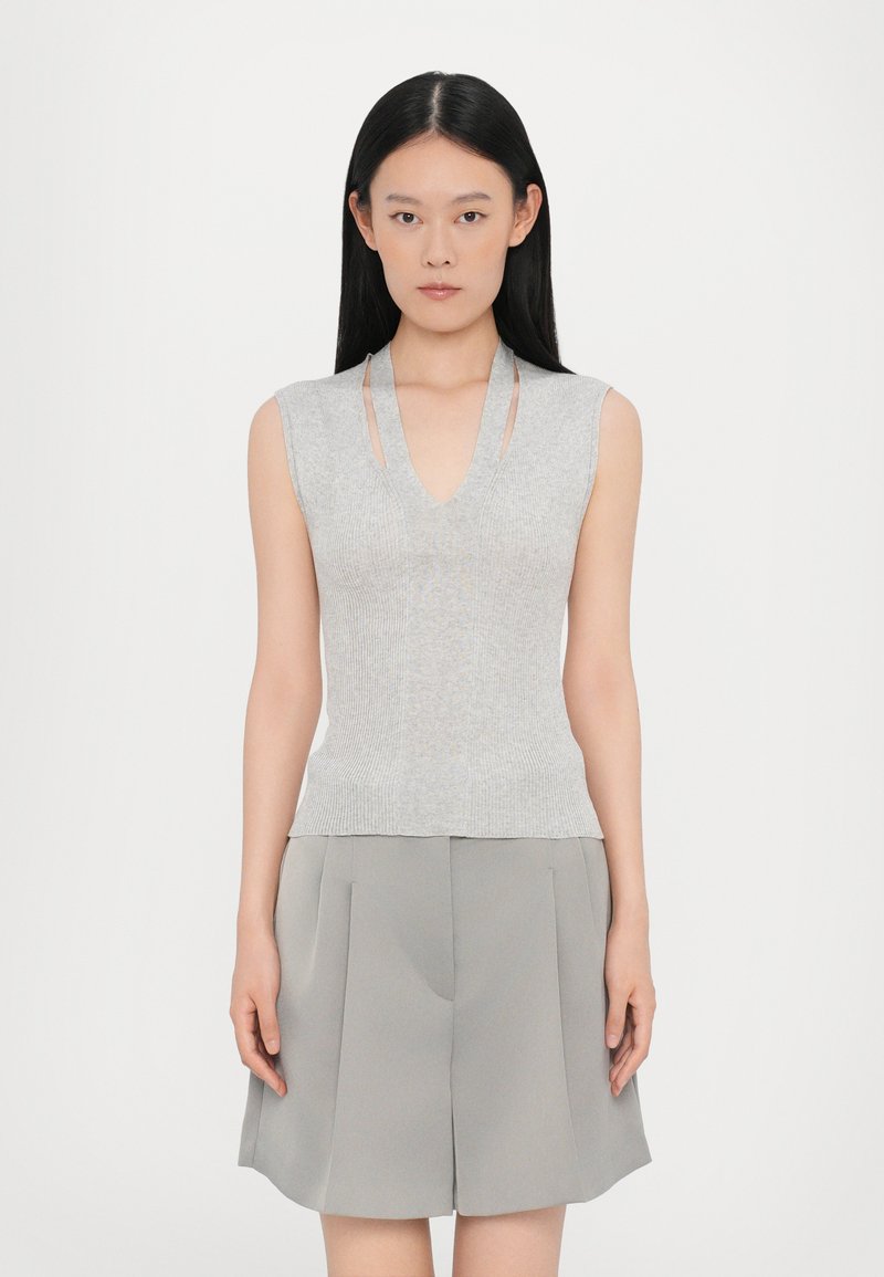 Top senza maniche grigio a coste con scollatura a V e dettagli a taglio, realizzato in materiale morbido. Abbinato a pantaloni corti plissettati grigio chiaro.