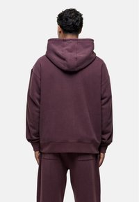 Kaptur z ciemnego burgunda, wykonany z miękkiego materiału. Posiada luźny krój, opadające ramiona i kieszeń typu kangurka.