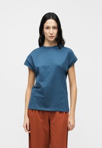 Μπλε βαμβακερό t-shirt με κοντά καπελάκια στα μανίκια και στρογγυλή λαιμόκοψη, σε συνδυασμό με παντελόνι ευρύχωλο σε σκουριά απόχρωση. Απλός, καθαρός σχεδιασμός με χαλαρή εφαρμογή.