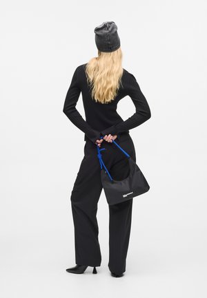 Czarny prążkowany top z długim rękawem, czarne spodnie w stylu szerokich nogawek, torba w wielokolorowy wzór z niebieskim paskiem oraz czarne botki na obcasie. Model odwrócony plecami.