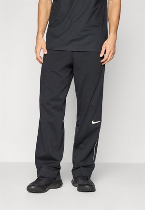 Pantalon de sport noir à coupe décontractée, avec un logo Nike blanc sur la jambe gauche et des zips aux chevilles pour des ouvertures ajustables.