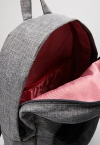 Zaino grigio con texture, con fodera interna a strisce rosse e bianche, aperto per mostrare il comparto imbottito per laptop e le tasche interne.