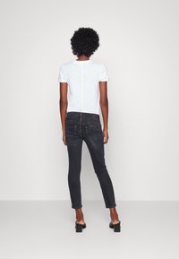 Jeans ajustados negros de talle alto, con detalles en los bolsillos traseros y una etiqueta de cuero marrón. Combinados con una camiseta blanca de manga corta.