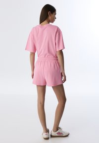 Camiseta de algodón rosa con mangas cortas y pantalones cortos rosa a juego, con una cintura elástica. El calzado es blanco con detalles en rosa.