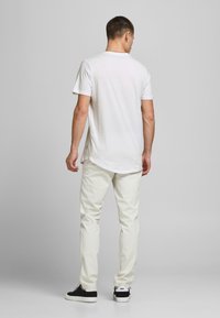 Biela bavlnená tričko s krátkymi rukávmi, zakriveným lemom, spárované s úzkymi svetlo béžovými nohavicami a čiernymi teniskami. Jednoduchý a neformálny outfit.