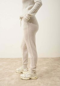 Světlé šedé pletené jogger kalhoty s bočními kapsami, žebrovaným pasem a šňůrkou. Spárováno s krémovými teniskami s texturovaným povrchem.