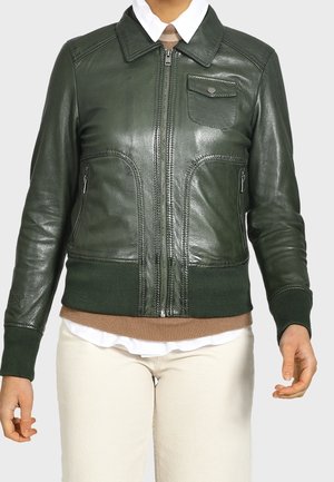 Dunkelgrüne Lederjacke mit Frontreißverschluss, Reißverschlusstaschen an den Seiten, Brusttasche mit Klappe, gerippten Bündchen und Saum, getragen über weißem Hemd und beigefarbenem Pullover.