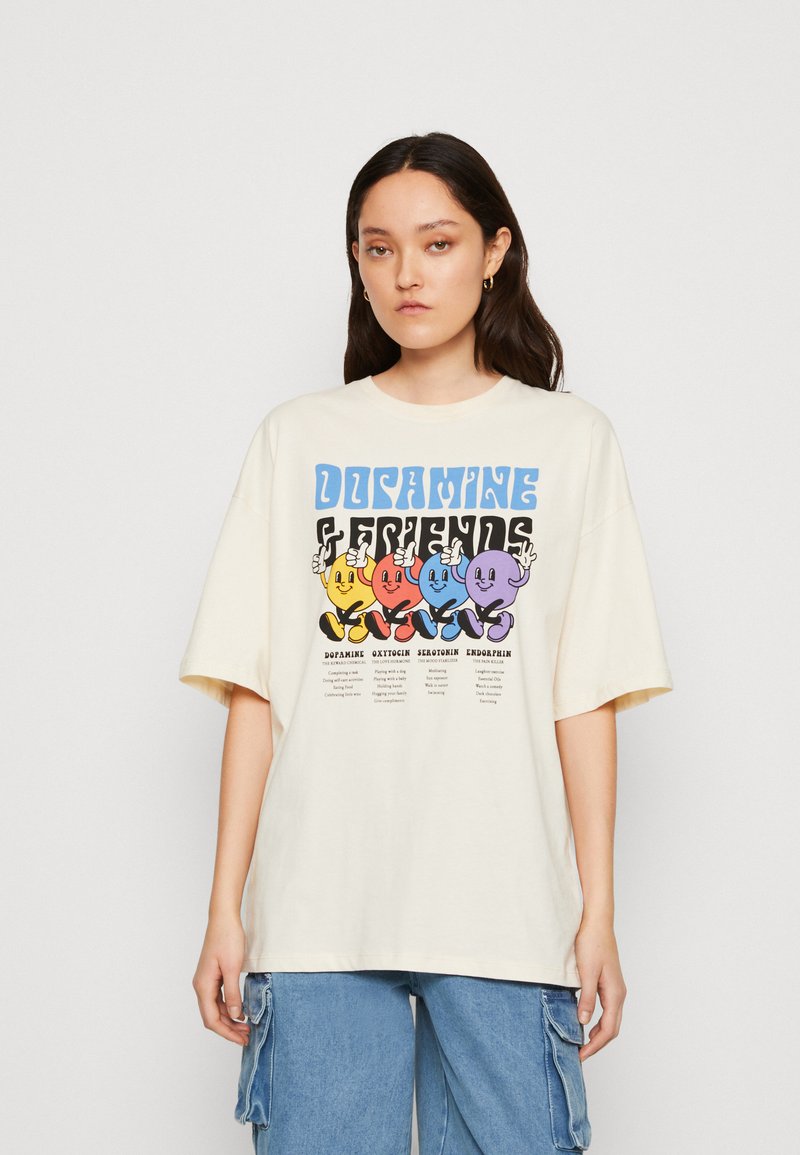 Krämfärgad oversized t-shirt med en grafisk tryck som visar färgglada tecknade ansikten, märkta med termer som dopamin och serotonin.