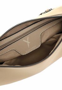 Beež koti sisestruktuuril on sile ja pehme tekstuur, millel on lukuga tasku ja logopaik. Lukk on must ja nähtavate õmbluse detailidega.