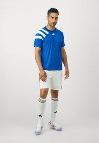 Blå treningsskjorte med hvite detaljer, hvite shorts med svarte striper, knelange hvite sokker og lyseblå fotballsko.