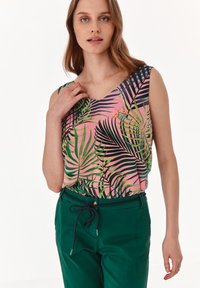 Top senza maniche con sfondo rosa e motivo di foglie tropicali verdi e nere; abbinato a pantaloni verde scuro e vita stretta.