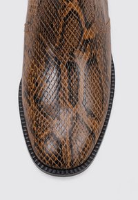 Bottine en cuir à motif serpent brun, avec un bout pointu, présentant une texture lisse et un bord noir le long de la semelle.