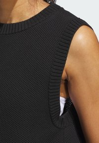 Czarny top bez rękawów z fakturowanym wzorem dzianiny, z prążkowanym dekoltem i otworami na ramiona, prezentujący luźny krój oraz warstwową białą bazę pod spodem.