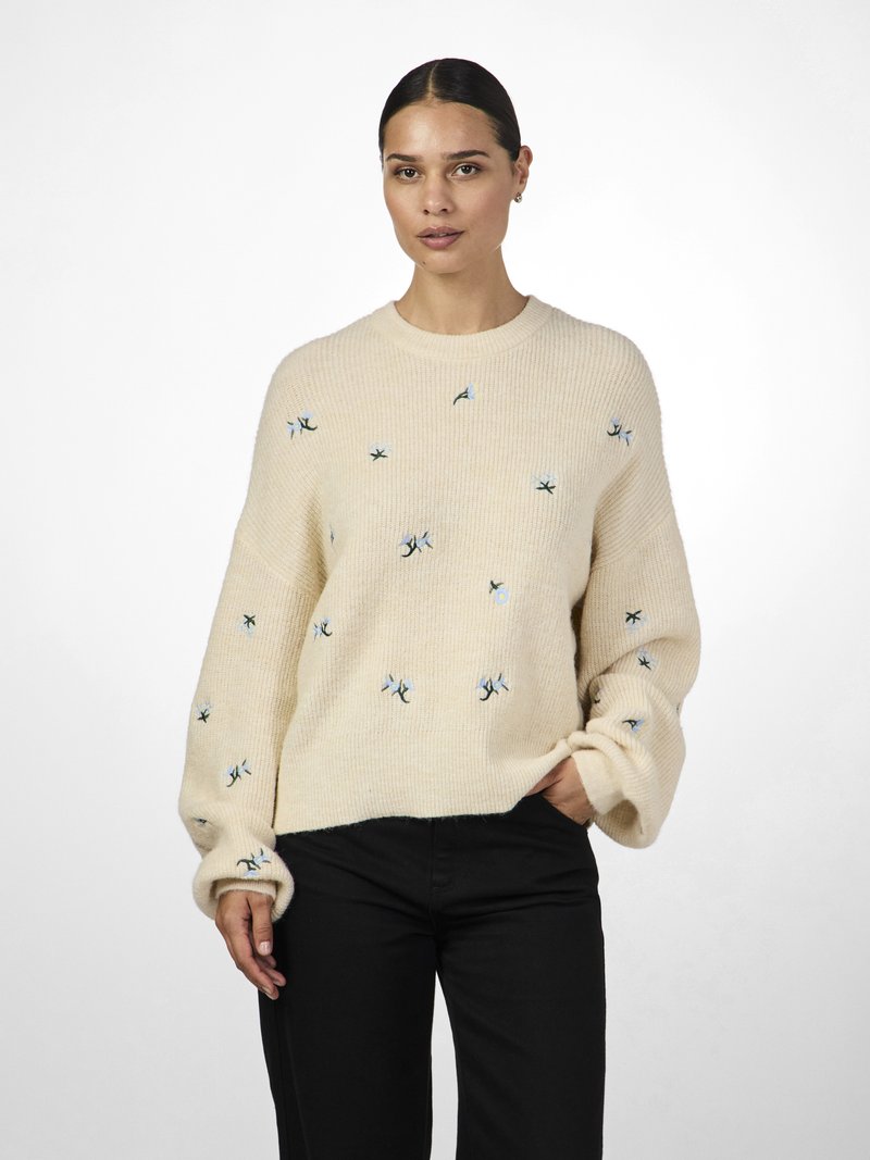 Hellbeige gestrickter Pullover mit langen Ärmeln, verziert mit blauer und schwarzer Blumenstickerei. Lockerer Schnitt mit gerippten Bündchen und Halsauschnitt.